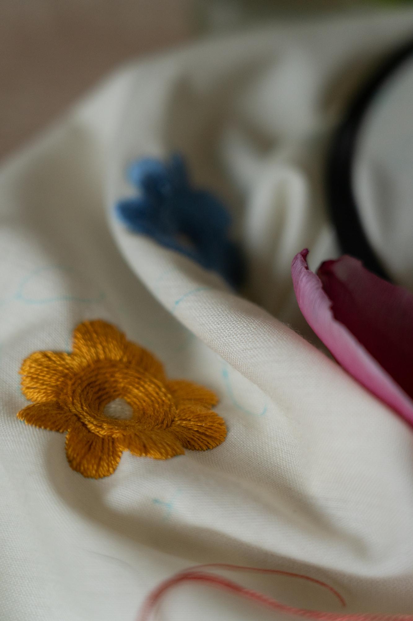 Mano che ricama un fiore su cotone beige